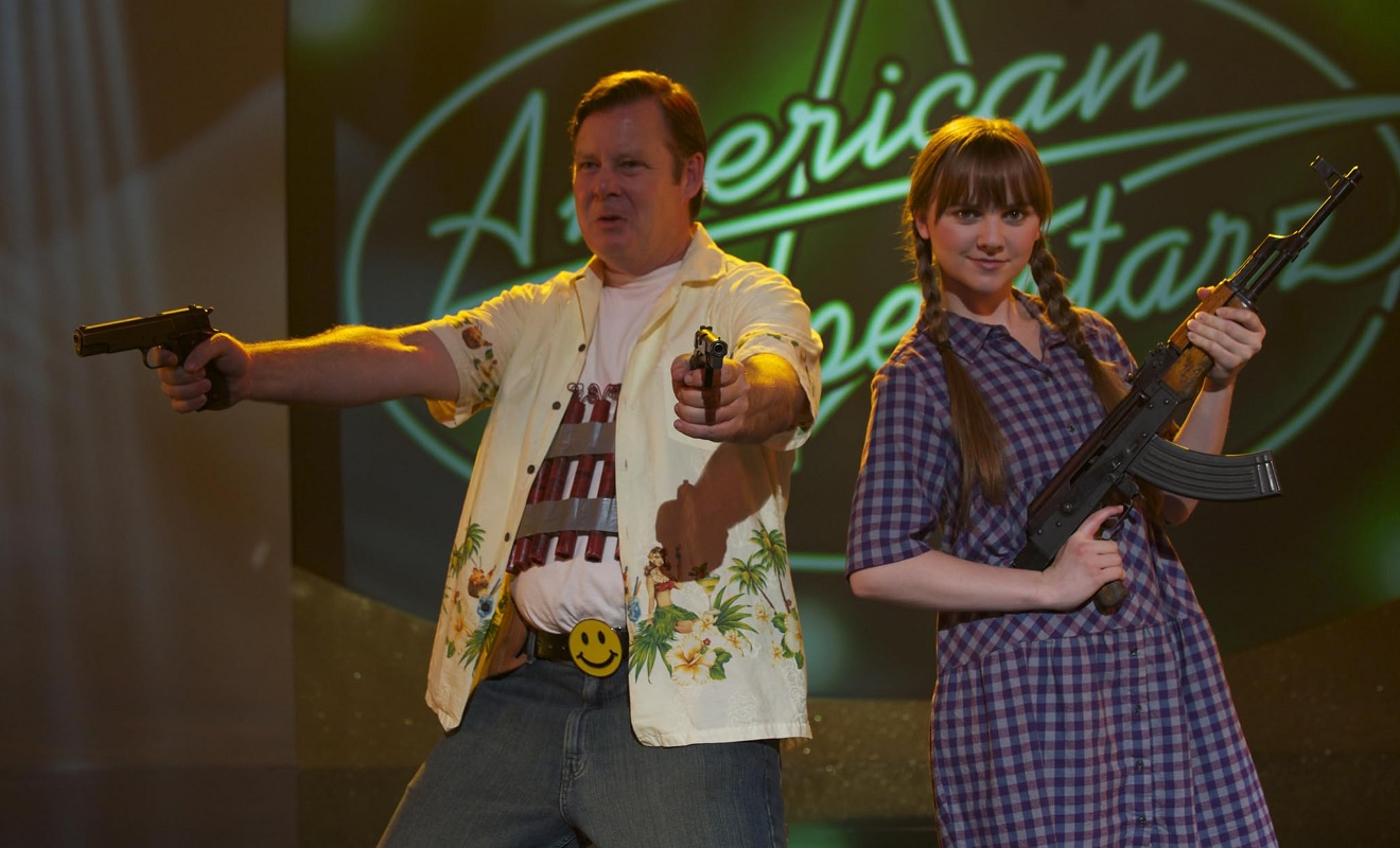 Screenshot from the movie God Bless America. The characters Frank Murdoch and Roxy Harmon are holding guns, with an American Idol sign right behind them.